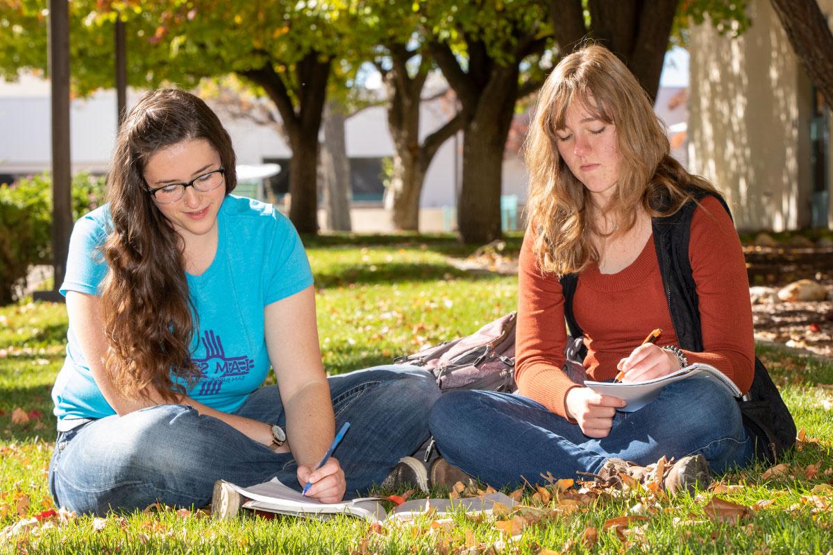 Two SJC students do class work while sitting outside on the lawn